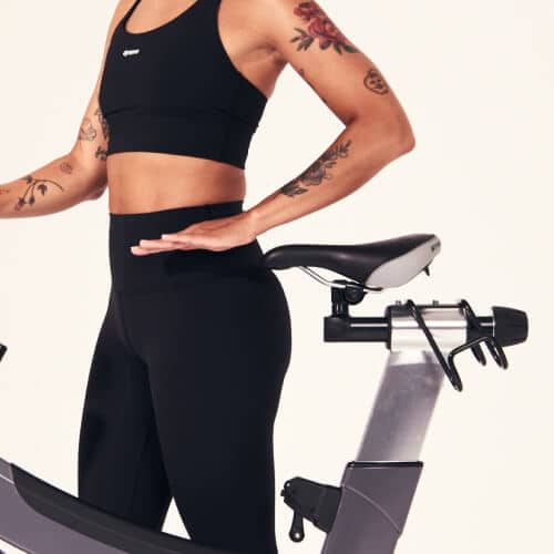 Femme en tenue noire, main posée sur la selle d’un vélo de cycling